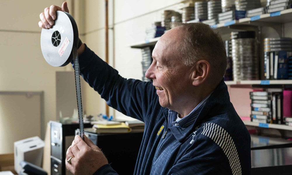 Terry Gurnett holds a film canister with unspooled film to the light. 